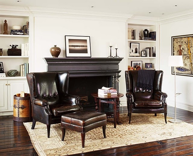 A sophisticated living room with all neutrals, dark leather furniture, a dark fireplace plus built in storage units