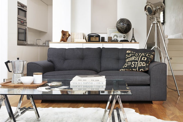 A contemporayr living room with a grey sofa, a glass coffee table, a floor lamp, some storage units and a rug
