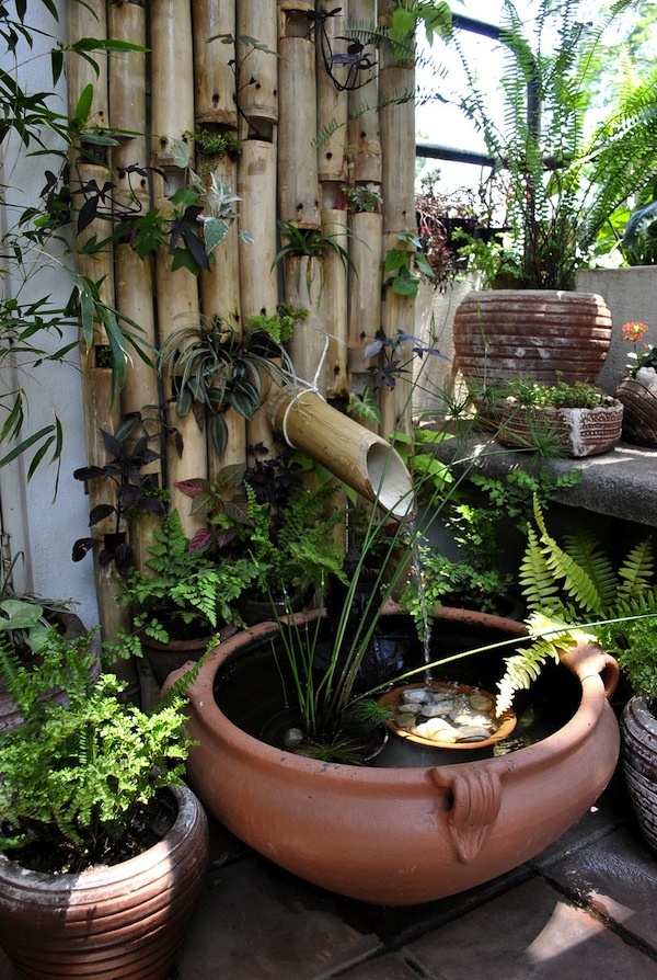 A Japanese inspired bamboo wall with greenery, a porcelain bowl and pebbles and greenery plus a bamboo fountain