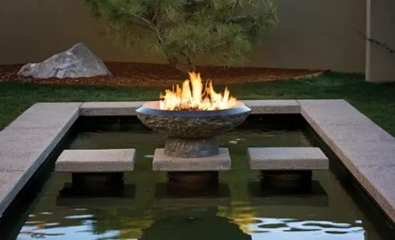 a modern pond clad with stone, with stone steps and a fire bowl over it is a gorgeous idea for a modern outdoor space with style