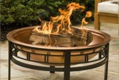 a large and beautiful copper fire bowl on a comfortable black metal stand is a lovely solution for many backyards, it will add a soft touch of color to the space