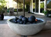 a neutral stone fire bowl with black pebbles and stone spheres will add interest and a modern feel to your outdoor space for sure