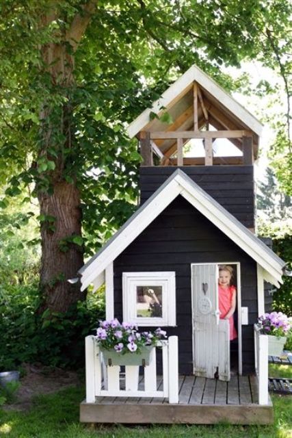 A black and white Nordic kids' playhouse with a small deck and potted blooms is a cool idea for a Scandi inspired garden