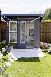 a small black and white kids’ playhouse with large windows and sliding doors, a colorful garland, blooms and greenery and a striped rug