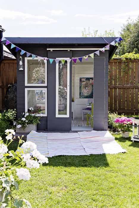 a small black and white kids' playhouse with large windows and sliding doors, a colorful garland, blooms and greenery and a striped rug