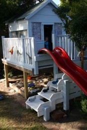 a small white kids’ playhouse with a large ladder, a red slide, printed curtains is a great place to play and to have some personal space