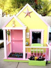 a super colorful kids’ playhouse with yellow walls and a pink door, a green bench and a planter with greenery is fun and cool