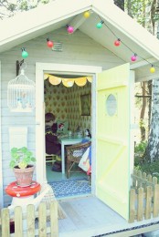 a pastel kids’ playhouse with vintage furniture, colorful garlands, a cage, potted blooms and greenery and colorful garlands
