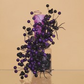 a purple candle held by blakc and purple berries and black spiders for easy and fun Halloween decor