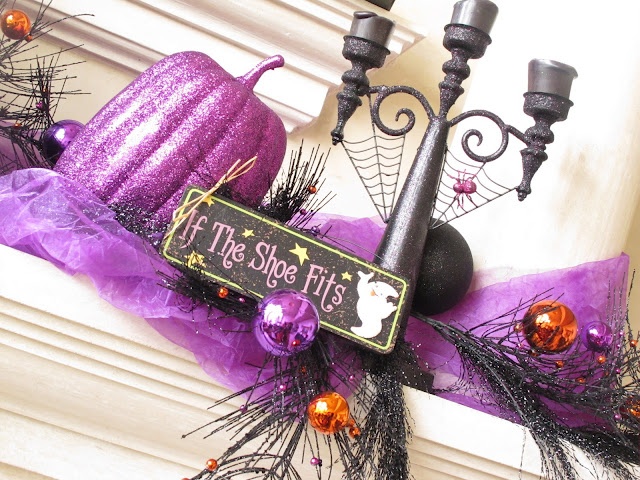 A Halloween mantel with a black candelabra, white candles, purple fabric and pumpkins, bold ornaments on branches is a cool idea