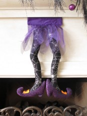 black and purple spiderweb witch’s legs hanging over the fireplace is a very catchy and cool Halloween decor idea