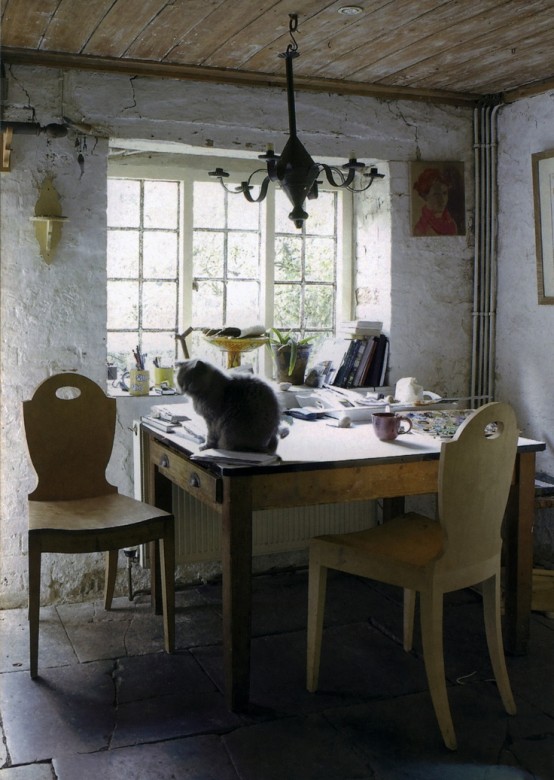 a rustic vintage home office with white plaster walls, wooden furniture and chairs, a vintage lamp and some artworks