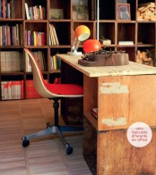 a modern rustic home office with a large shelving unit with books, a vintage wooden desk, a red chair, orange lamps