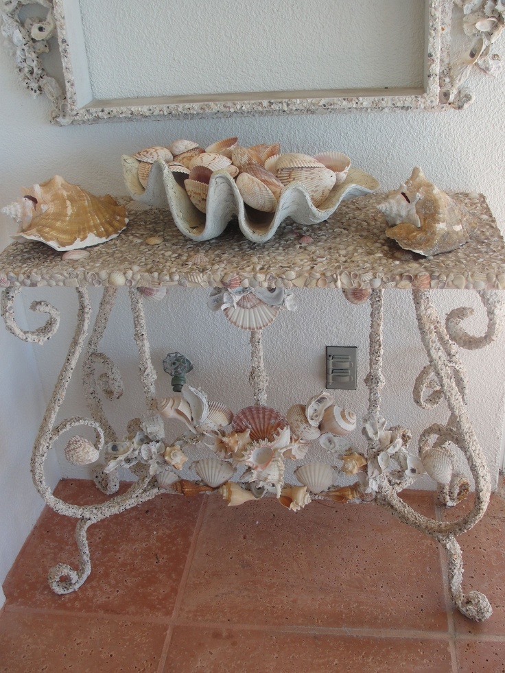 A refined sea inspired console table with lots of seashells covering it and with seashells on top for a beach entryway