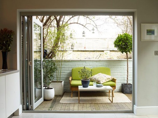 a small and cozy mid-century modern terrace with potted greenery,a  green sofa, a rug and a small coffee table