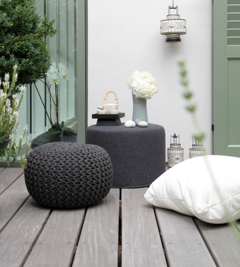 a small contemporary terrace with a couple of dark ottomans and pillows, lanterns and a tea set