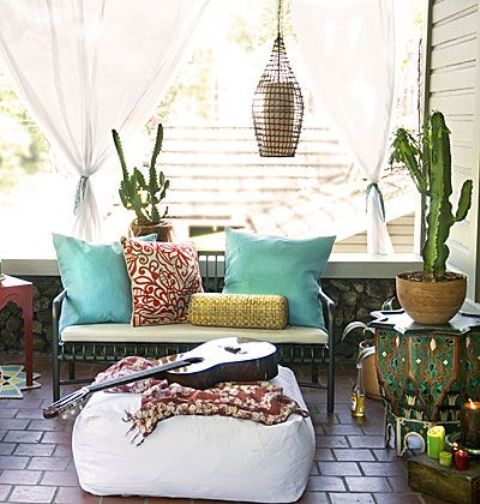 a small boho terrace with carved furniture, a white ottoman, a candle lantern and colorful textiles