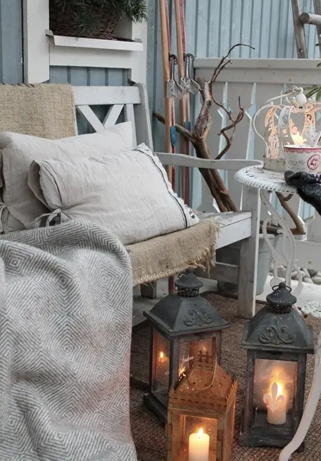 a small rustic terrace with whitewashed vintage furniture, candle lanterns, branches and skis