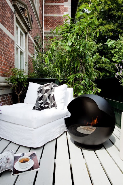 a small contemporary terrace with a black hearth, a white lounger and much greenery for freshness and privacy