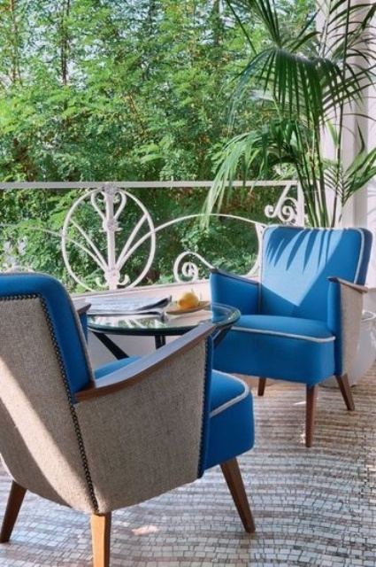 an elegant small terrace with blue upholstered chairs, a rug and a glass coffee table