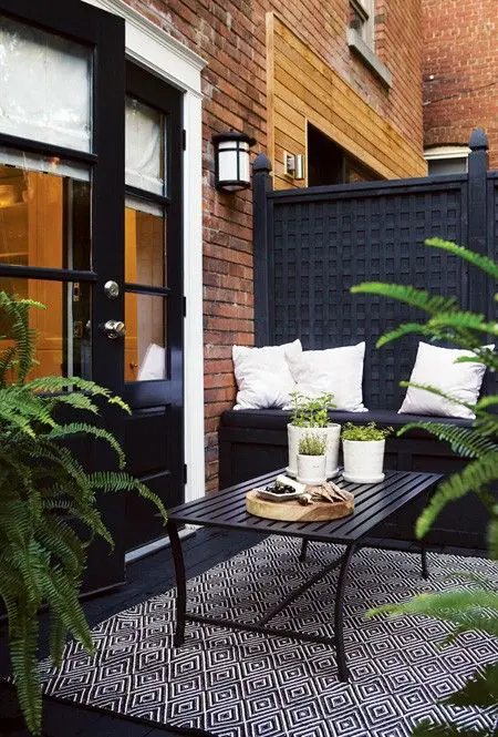 a moody small terrace with black furniture, rugs and lots of potted greenery to refresh the space
