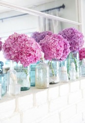 a bright summer mantel with bright pink hydrangeas in vases, seashells in jars
