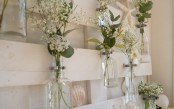 a white pallet with vases and bottles attached, with fresh blooms and seashells and starfish