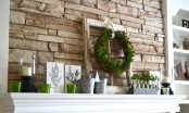 a rustic summer mantel with a greenery wreath and potted greenery, buckets, candle holders and posters