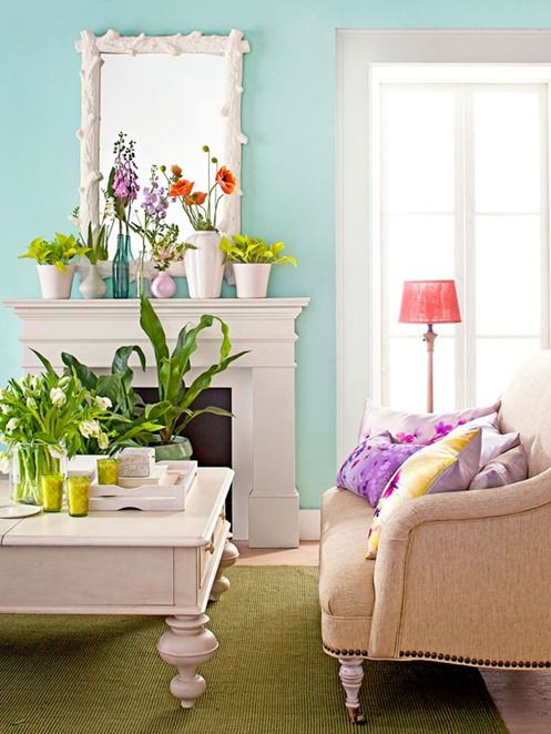 a bright summer mantel with colorful potted blooms and greenery on it and on the coffee table