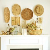 a cozy summer mantel with decorative baskets and trays, a straw hat, a basket with blooms and glass bottles and vases
