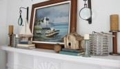 a seaside mantel with a sea artwork, boats, a bird house and nautical lanterns and candles