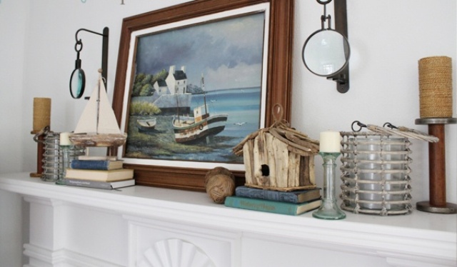 A seaside mantel with a sea artwork, boats, a bird house and nautical lanterns and candles