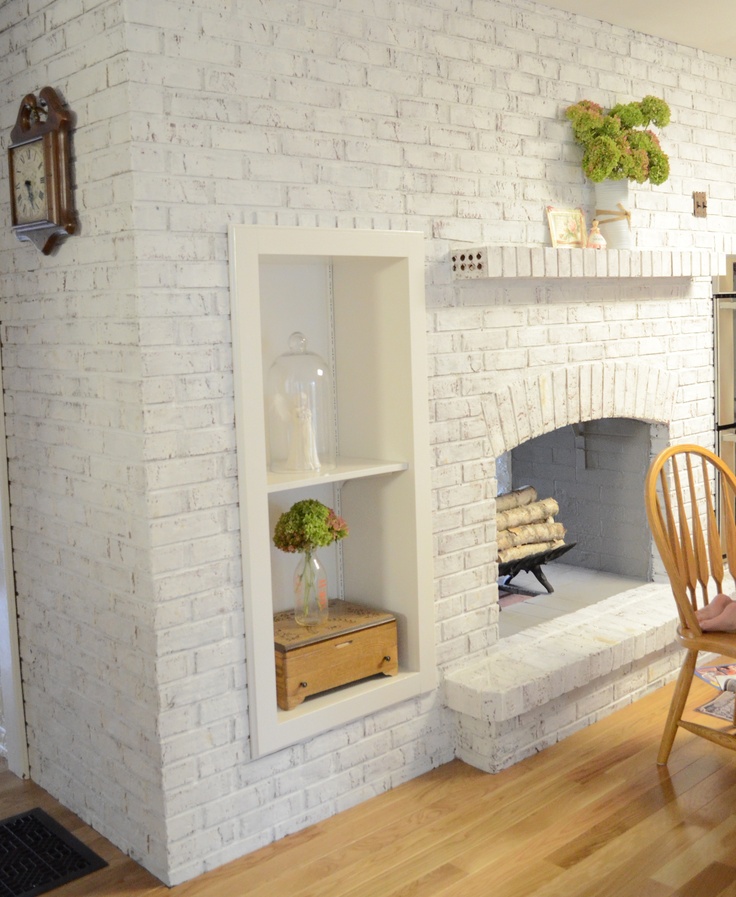 An oversized whitewashed brick non working fireplace with built in shelves and potted greenery is a stylish and cozy decoration