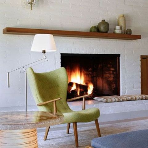 A mid century modern whitewashed fireplace with a simple mantel and a green chair next to it is stylish and elegant