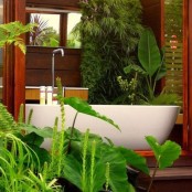 a half outdoor and half indoor bathroom clad with wood and with lots of tropical plants for a chic and lively look – completely connected with nature