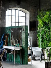 an industrial bathroom done with concrete, with an emerald green tile space divider and a real living wall that refreshes the whole space at once