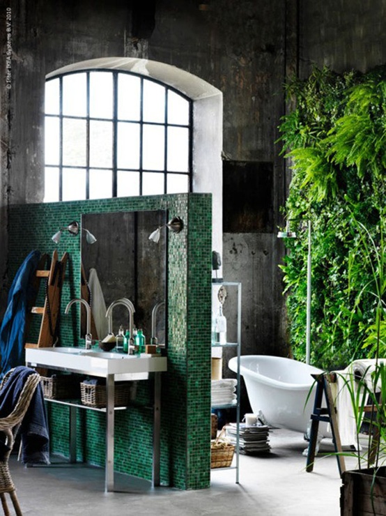 an industrial bathroom done with concrete, with an emerald green tile space divider and a real living wall that refreshes the whole space at once