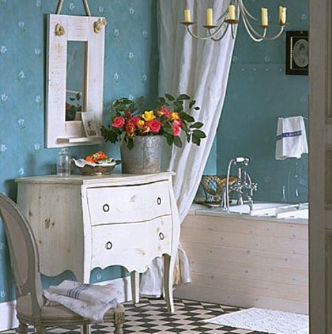 A vintage inspired bathroom with blue wallpaper walls, refined white furniture and some blooms in a bucket planter for a rustic feel