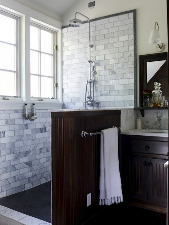 an elegant bathroom clad with marble subway tiles, with a dark half wall and a matching vintage vanity looks chic