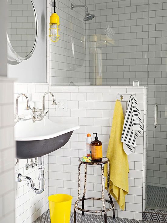 A mid century modern bathroom clad with white subway tiles, with a half wall, a vintage sink and touches of yellow for a brighter look