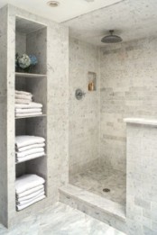 a neutral contemporary bathroom clad with white marble tiles, with a half wall for the shower space and built-in shelves