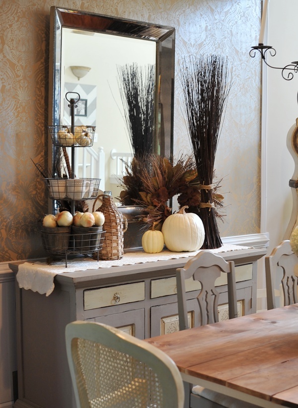 A console in the dining room styled for the fall   with a dried herb wreath, branches, white pumpkins and a stand with pumpkins and faux apples