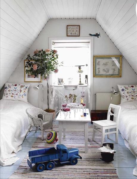 a white shabby chic attic bedroom with floral pillows, a gallery wall, a statement plant, white furniture, a striped rug and toys