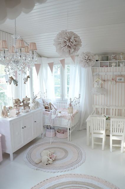 a blush and white shabby chic kid's room with pink and blush textiles, lamps and garlands, a crystal chandelier, and a metal bed