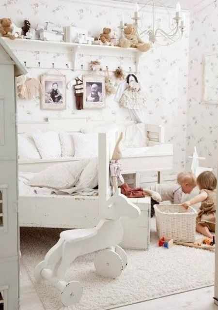 a white shabby chic kid's room with white furniture and a chandelier, floral wallpaper, a shelf with toys and baskets for storage
