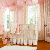 a shabby chic kid’s room with pink walls, pink paper lamps, floral bedding and textiles