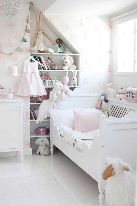 a white and blush shabby chic kid's room with floral wallpaper, chic white furniture, built-in shelves and lots of toys and a crystal chandelier over the space