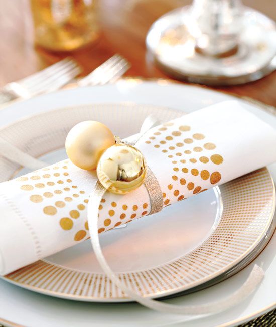 a modern neutral NYE place setting with white porcelain, a printed napkin with gold ornaments attached is a lovely and bold idea