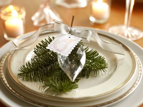 a simple and stylish NYE place setting with neutral plates, evergreens, a large crystal as a favor and candles around