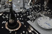 a black and silver NYE party tablescape with silver glitter placemats, a table runner and silver cutlery, rhinestones and disco balls on the table